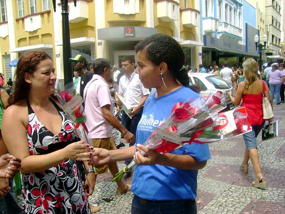 Foto de mulher recebendo uma rosa da funcionária do Sindicomércio