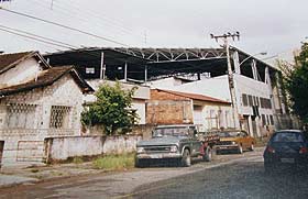 Foto antiga de uma rua com um carro estacionado e um galp?o antigo