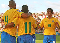 Foto de dois jogadores da Sele??o Brasileira abra?ados e Kak? indo em dire??o a eles, sorrindo